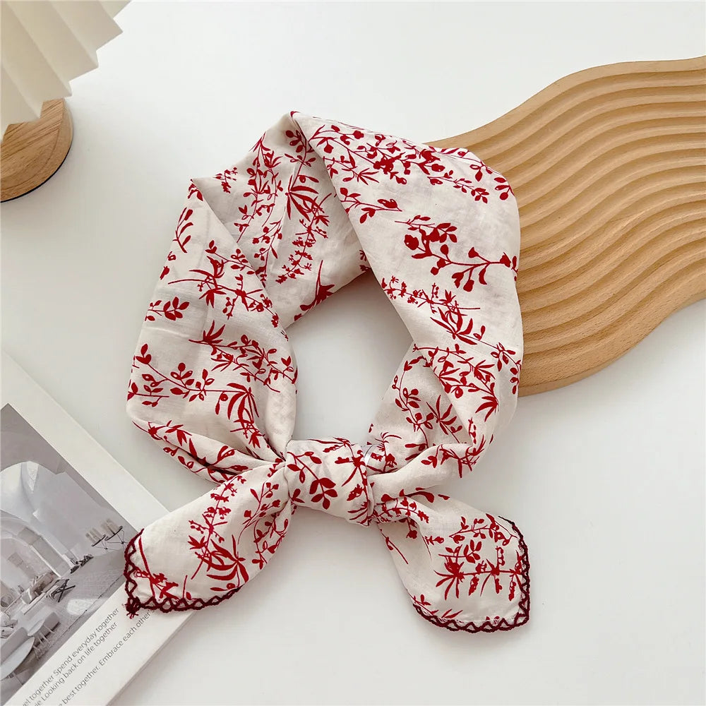 Gros plan d'un foulard en coton floral rouge noué en nœud, exposé sur une surface claire.