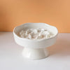 Un bol en céramique blanche à lent alimentaire rempli de nourriture blanche est exposé sur une surface claire sur fond orange