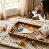 A wooden scraper for reusable cat food pouches resting on a beige woven mat with feathers and a small ball.