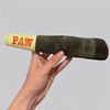 A hand holds a long, cylindrical plush toy dog chew with the word PAW printed on the end.