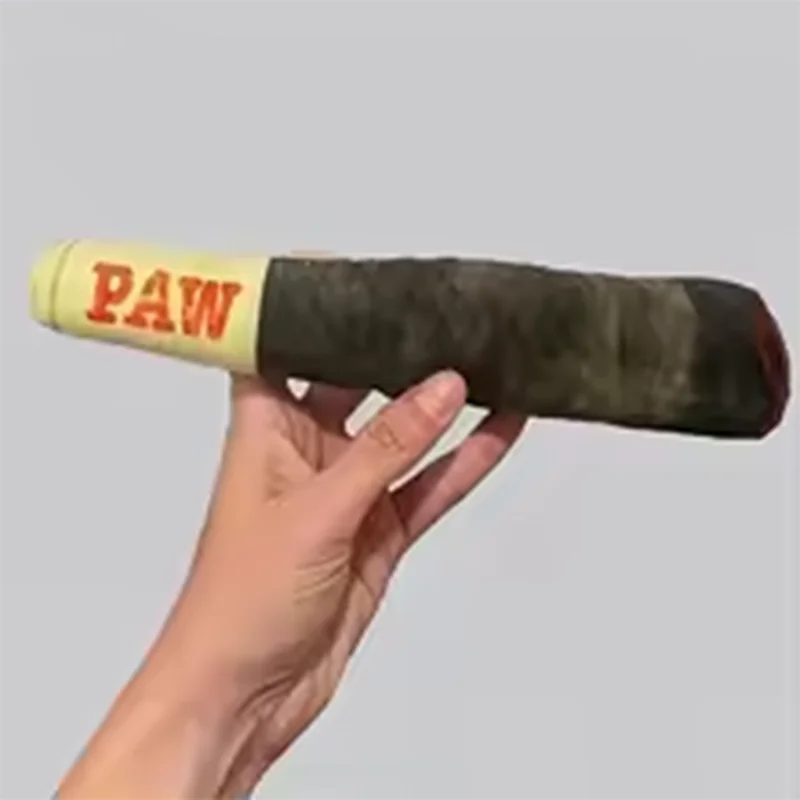 A hand holds a long, cylindrical plush toy dog chew with the word PAW printed on the end.