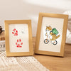 A wooden photo frame displays a paw print design, featuring a cat and a dog riding a green bicycle.