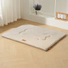 A beige waterproof dog bed mat with cushioned support placed on a light wooden floor.