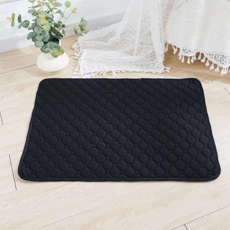 Black quilted reusable washable pet training mat placed on a light wooden floor next to a white lace fabric.