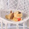 A soft, tan plush comfort toy shaped like a dog with floppy ears and an orange heart detail sitting on a white woven chair.