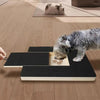 A wooden dog nail scratching board with a treat box is placed on a light wood floor next to a cat and a dog.