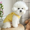 A fluffy white dog wearing a yellow waffle knit vest sitting on a woven surface.