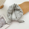 Foulard en coton à motif gris noué en nœud posé sur un objet en bois clair.