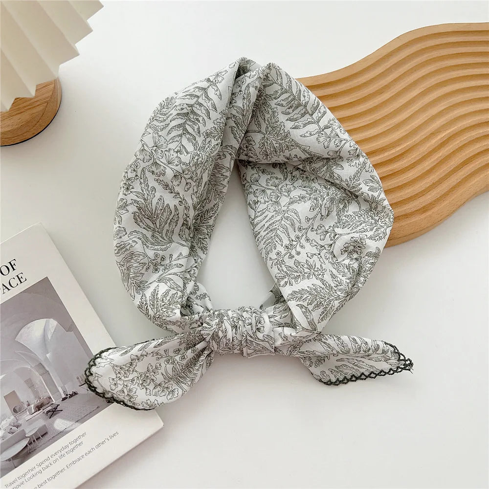 Foulard en coton à motif gris noué en nœud posé sur un objet en bois clair.