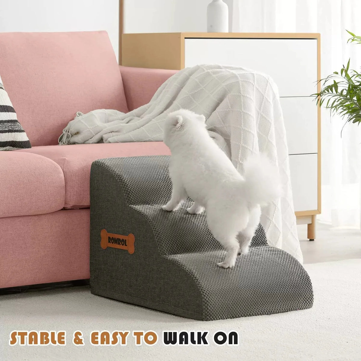 A white pet is walking on gray foam stairs with a white non-slip cover in a bright living room setting.