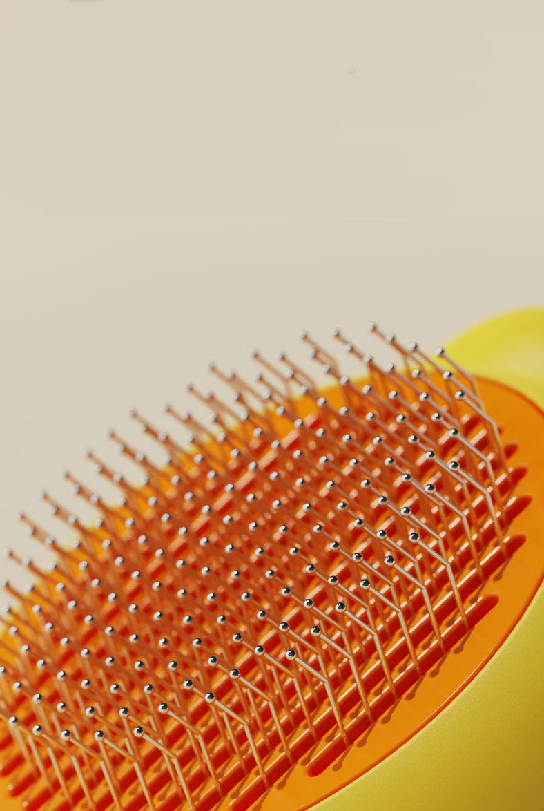 Close-up of an orange pet deshedding brush with numerous fine bristles and a yellow handle.