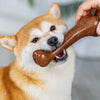 A small Shiba Inu dog is holding a brown natural wood chew toy in its mouth.