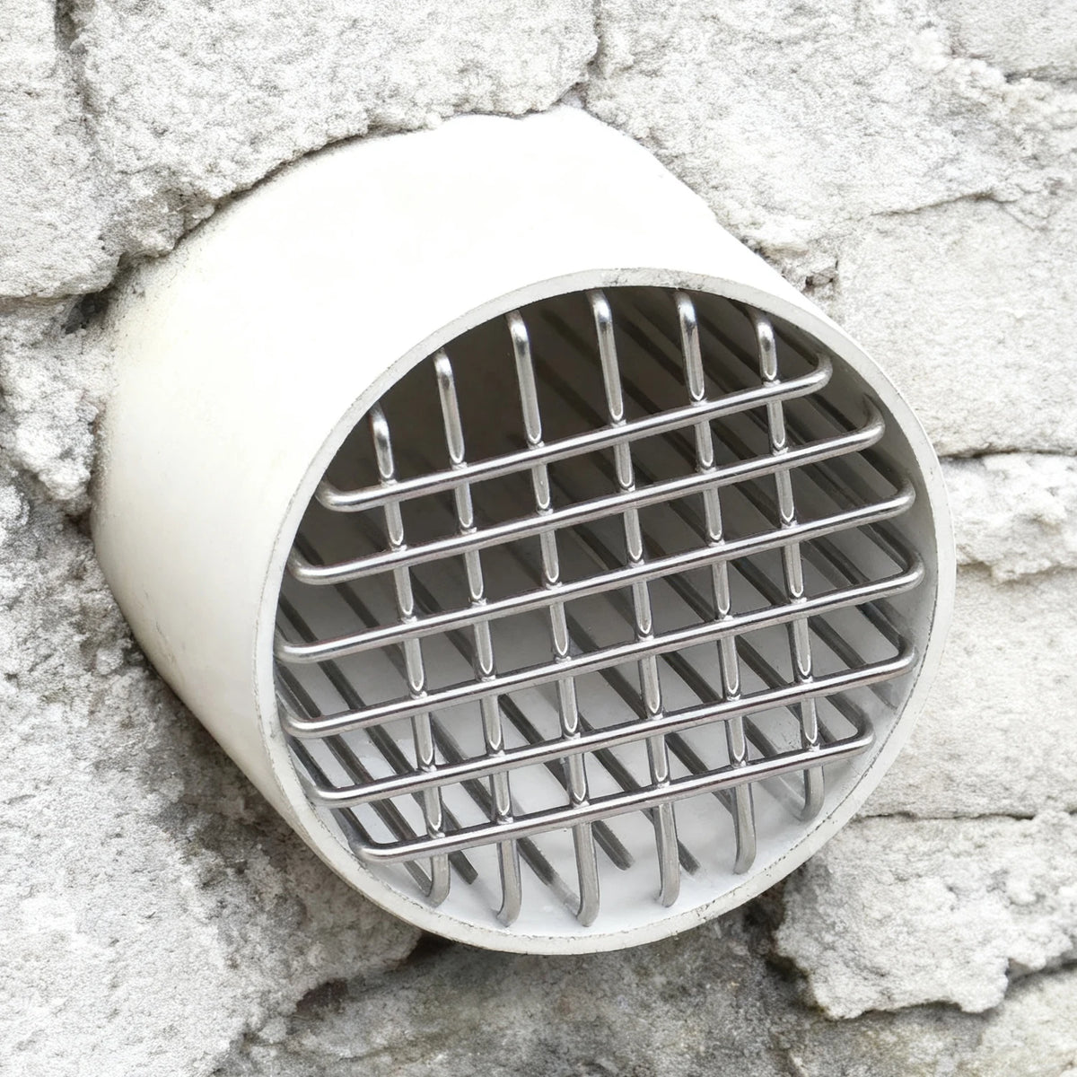 Tapa de malla para desagüe de suelo redondo de acero inoxidable contra una pared de piedra rugosa.