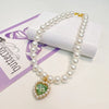 A delicate pearl necklace with a green gemstone pendant displayed on a white box.