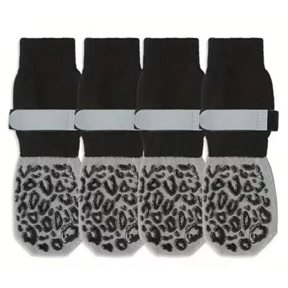 A set of four black anti-slip dog socks with leopard print paw protection and white wrist bands.