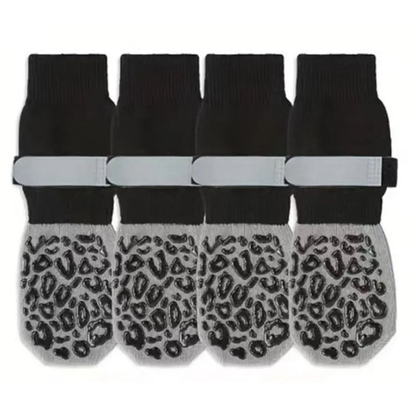 A set of four black anti-slip dog socks with leopard print paw protection and white wrist bands.