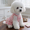 A fluffy white dog wearing a red and white striped ruffle hem knit dress sitting on a wooden surface.