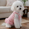 A fluffy white dog wearing a red and white striped ruffle hem knit outfit sitting on a light rug.