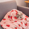 A pink blanket with a strawberry floral pattern is draped over a gray sofa.