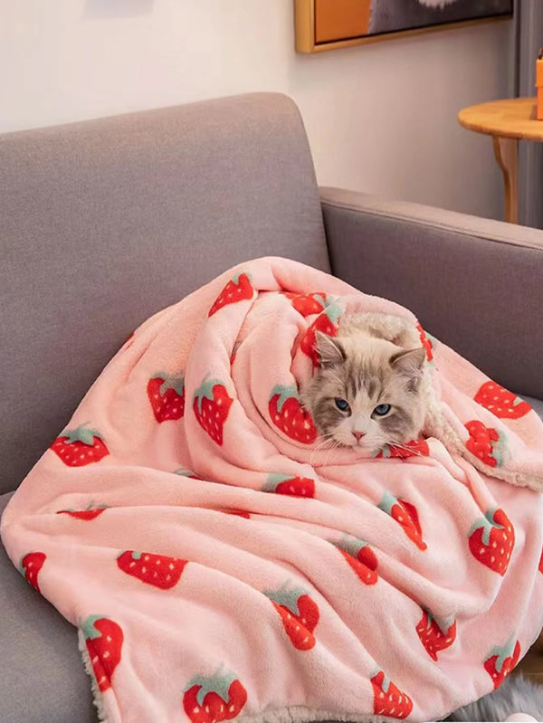 A pink blanket with a strawberry floral pattern is draped over a gray sofa.