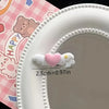 A close-up of a pink plate with a heart-shaped mini pet hair clip resting on the rim.