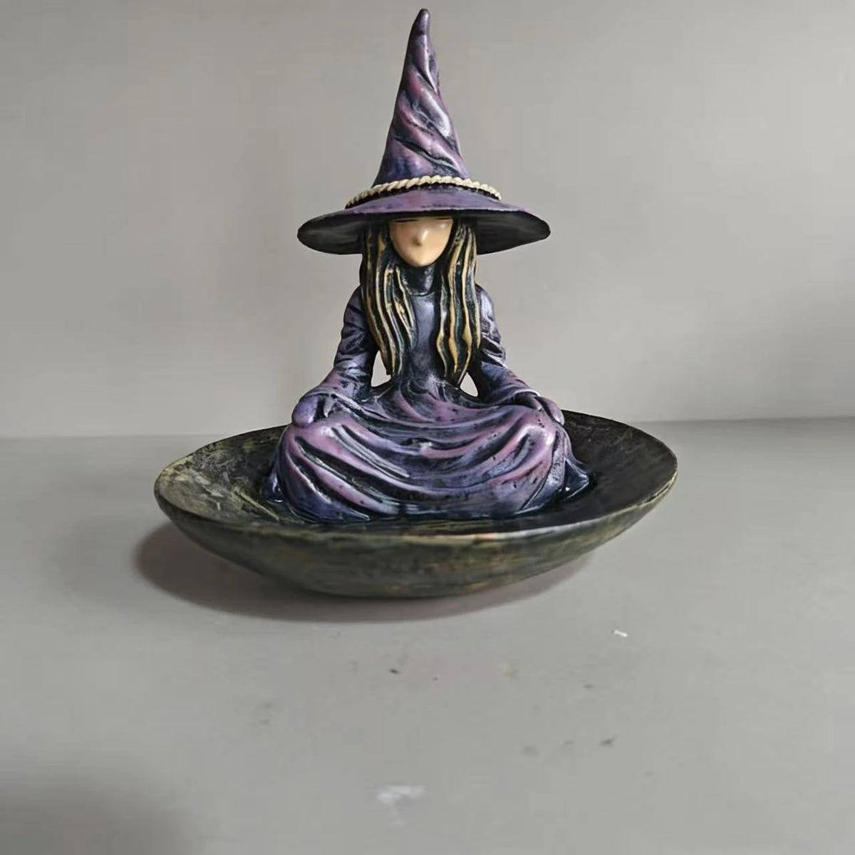 A resin figurine of a witch with a pointed hat and long hair sitting in a bowl.