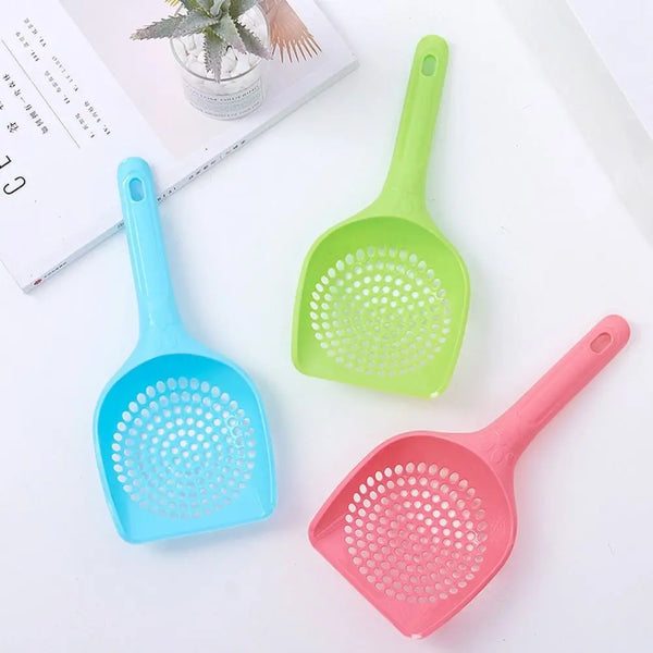 Three plastic cat litter scoops in blue, green, and pink colors are displayed on a white surface.