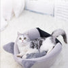 A fluffy gray cat is relaxing inside a plush, oval-shaped pet cave bed with a black trim.