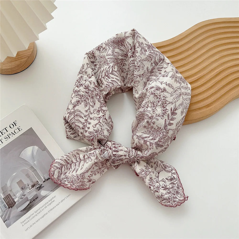 Écharpe en coton classique roulée à motif floral, présentée sur une surface blanche à côté d'une brochure.
