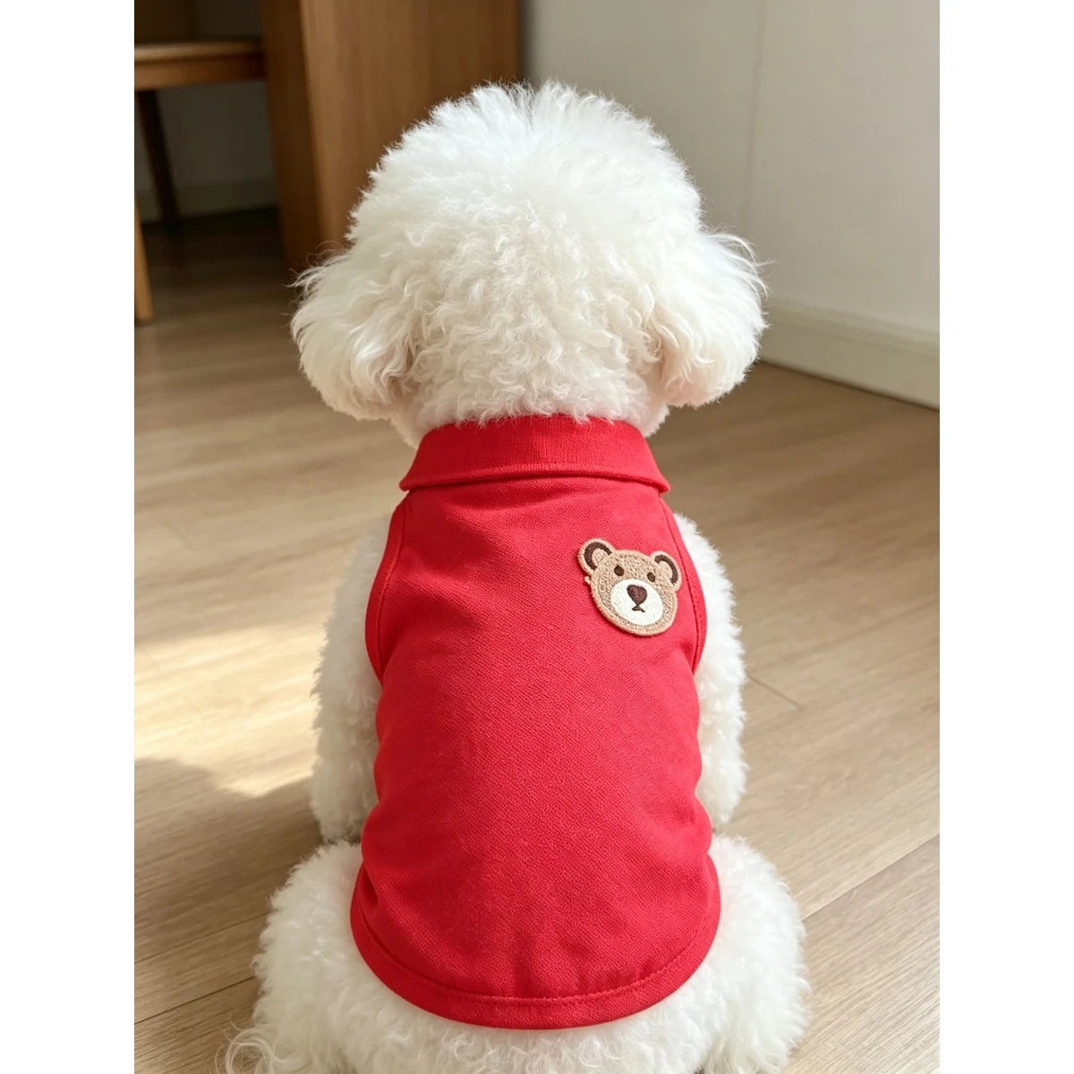 Un perro blanco y esponjoso vistiendo un chaleco rojo sin mangas con bordado de oso pardo en la espalda.