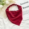 A deep red bohemian paisley triangle head scarf laid on a white fabric next to a piece of paper.