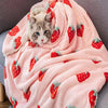 A pink blanket with a strawberry floral pattern is draped over a gray sofa, featuring a cat resting on the fabric.