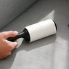 A hand is holding a white and black lint roller against a gray fabric surface.