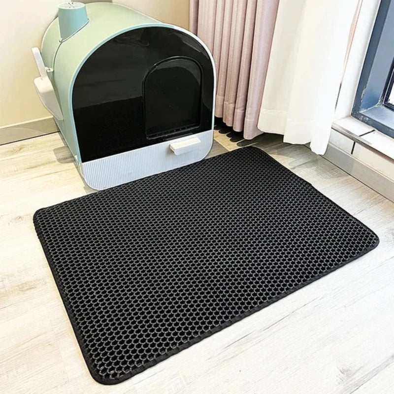 Un tapis de litière étanche noir est placé sur un plancher en bois clair devant une boîte pour chat vert clair.