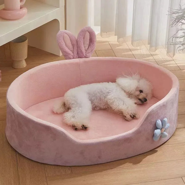 A pink, plush pet bed with a removable cover and raised guardrail, featuring a white fluffy dog resting inside.