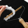 A hand holds a metal lint remover brush with gold-colored bristles, removing white lint from fabric.