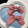 A red and white plaid fabric bow is displayed in a heart-shaped mirror frame.