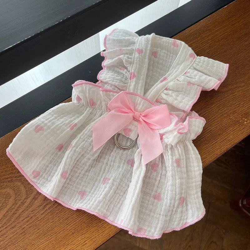 A white strawberry dog dress with pink polka dots and pink trim displayed on a wooden surface.