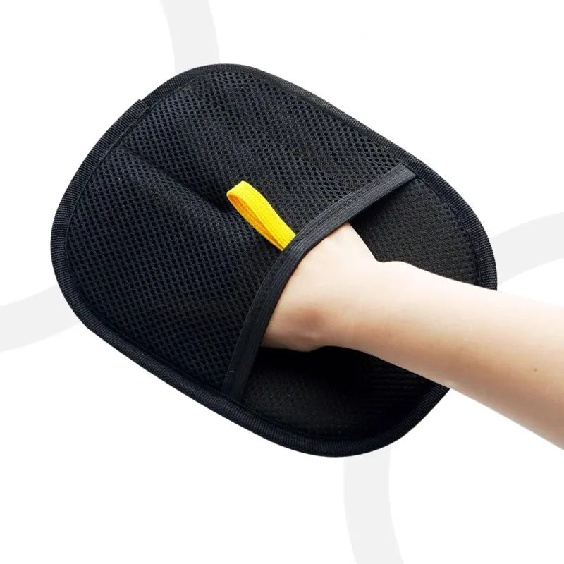 Eine Hand benutzt einen schwarzen Fellentfernungs-Grooming-Handschuh mit gelbem Griff auf weißem Hintergrund.