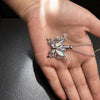 A silver butterfly ashes necklace is displayed on a person's hand.
