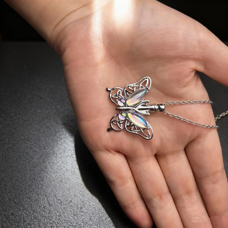 A silver butterfly ashes necklace is displayed on a person's hand.