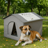 A brown and white dog is lying in front of a gray foldable waterproof insulated cat house in a grassy outdoor setting.