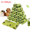 A stack of 10 to 100 rolls of biodegradable pet poop bags in light green with black paw prints, next to a dog and an open bag