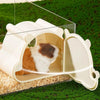 A white cartoon hamster hideout house with a viewing window is shown resting on green grass.