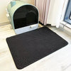 A black waterproof cat litter mat with a non-slip base is placed on a light wooden floor in front of a light green pet enclos