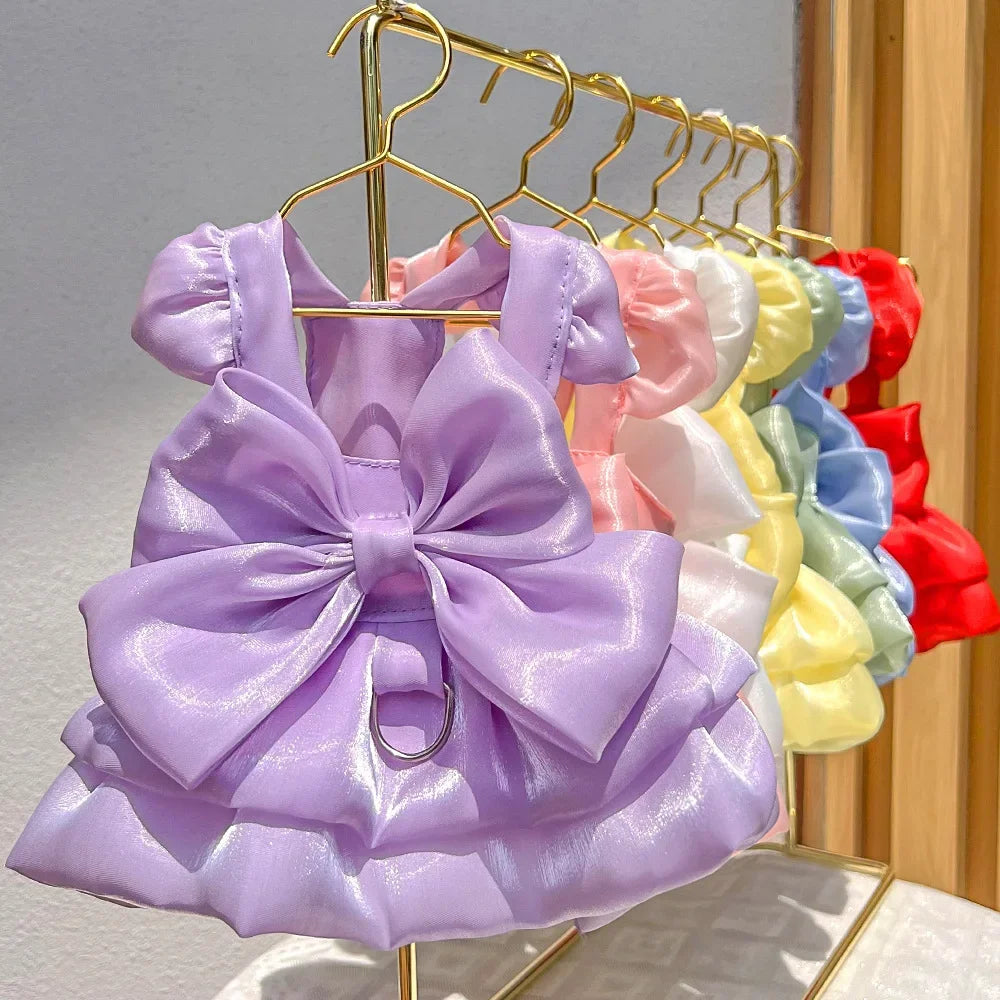 A purple solid color pet dress with a large bow and D-ring hanging on a gold hanger.