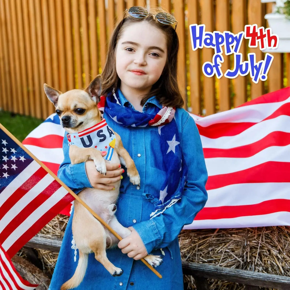 A young girl holds a small dog wearing a patriotic bandana in front of an American flag.
