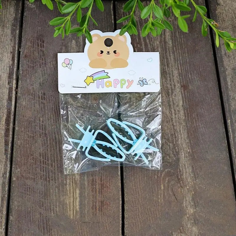 A clear plastic bag contains two light blue clip-on bird cage feeders with mounting brackets on a wooden surface.