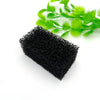 A rectangular block of black aquarium bio sponge filter media with green plant stems in the background.
