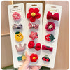 A hand holds a pack of five adorable flower-shaped baby hair clips in various colors and textures.